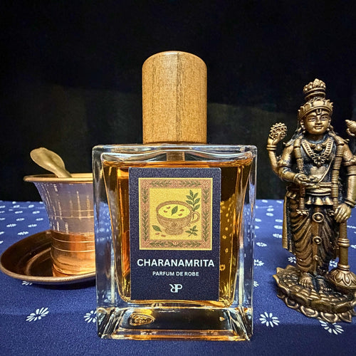 Fragrance bottle labeled 'Charanamrita' with a wooden cap on a dark background