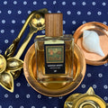 Perfume bottle labeled 'Ganga Arati' with gold and bronze elements against a blue background.