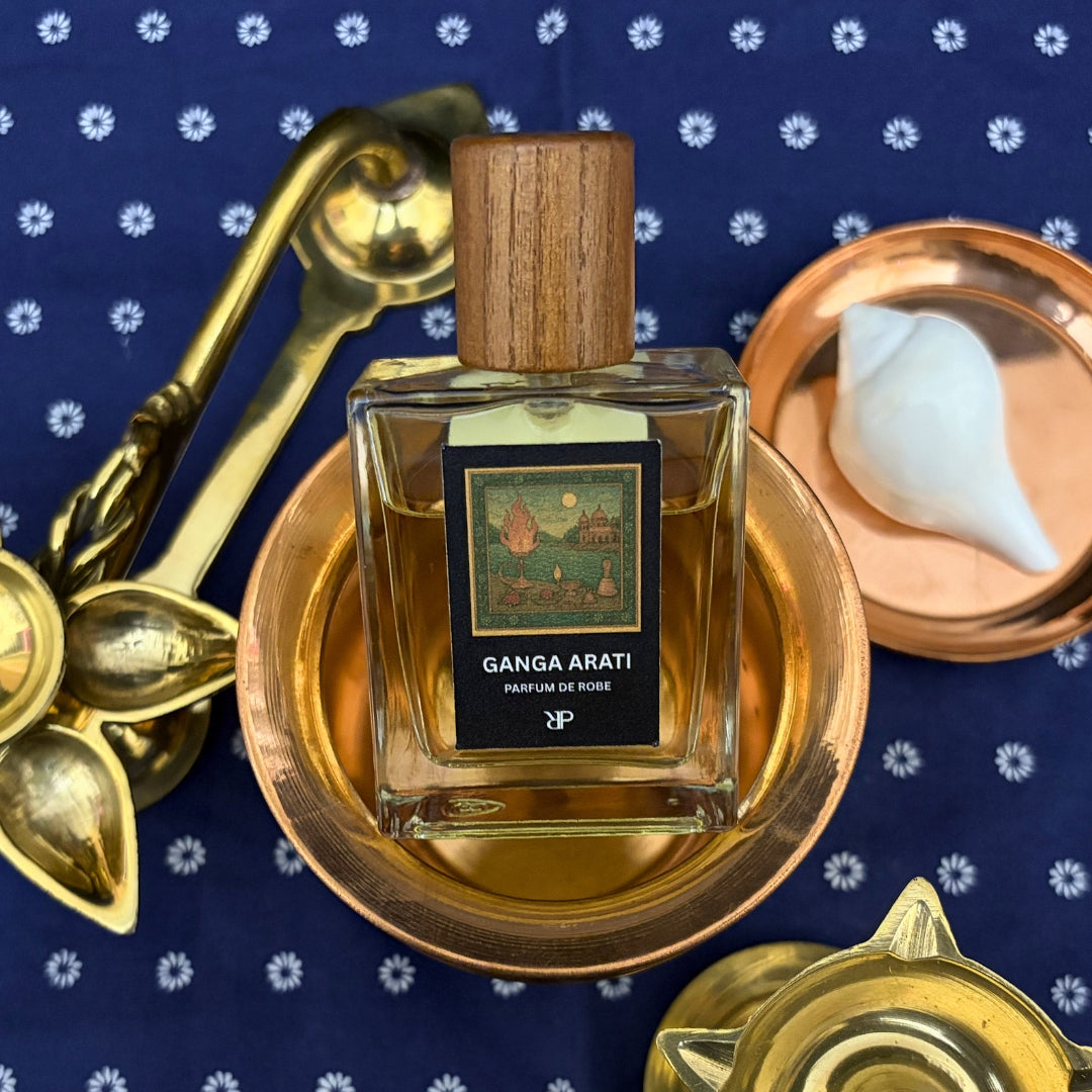 Perfume bottle labeled 'Ganga Arati' with gold and bronze elements against a blue background.