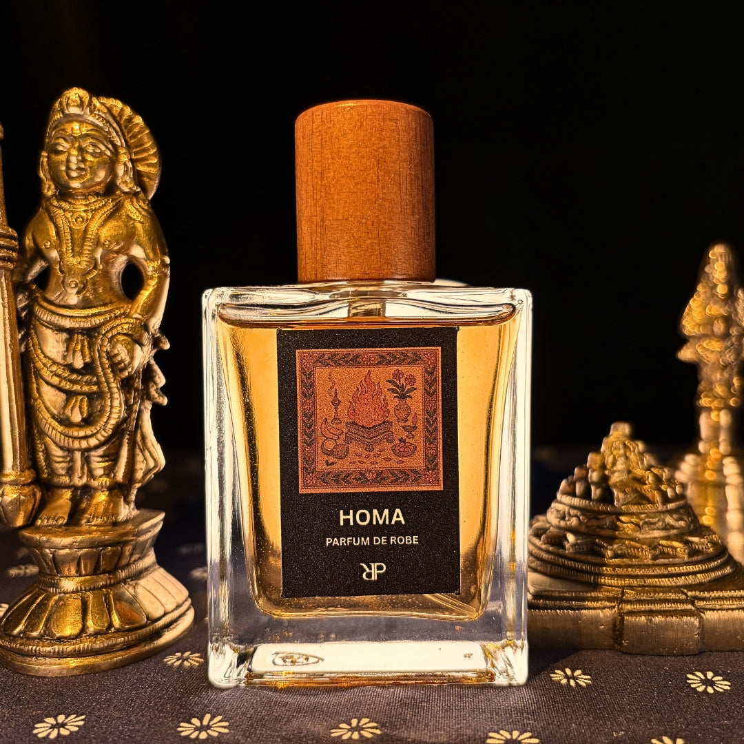 Fragrance bottle labeled 'Homa - Parfum de Robe' with decorative statues of Indian deities on a dark background