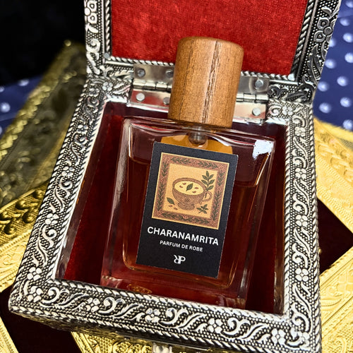 Fragrance bottle with wooden cap labeled Charanamrita, in an ornate silver and red box