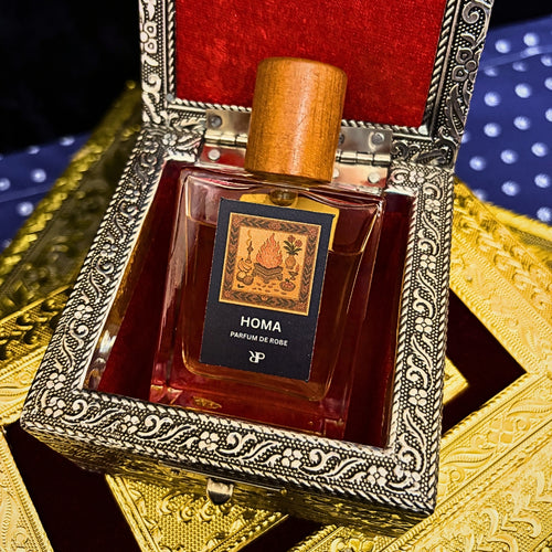 Fragrance bottle labeled 'HOMA - Parfum de Robe' in an ornate silver box on a gold and red background