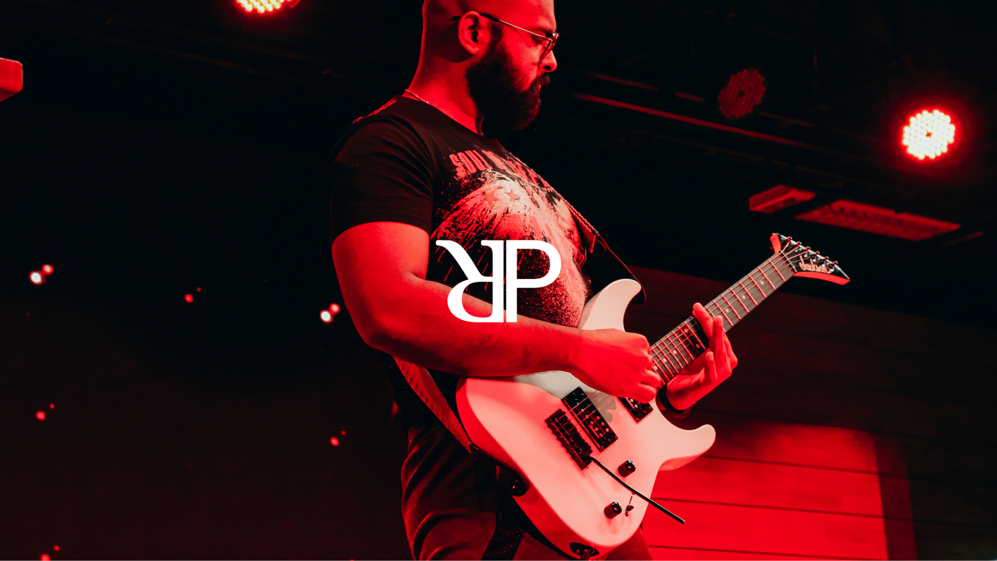 Picture of Dr. Parayan Sarkar, founder of Parayan O Rakkhoshgon, playing electric guitar live under red lights, with the "PR" logo of Parayan O Rakkhoshgon on top of the picture in white.